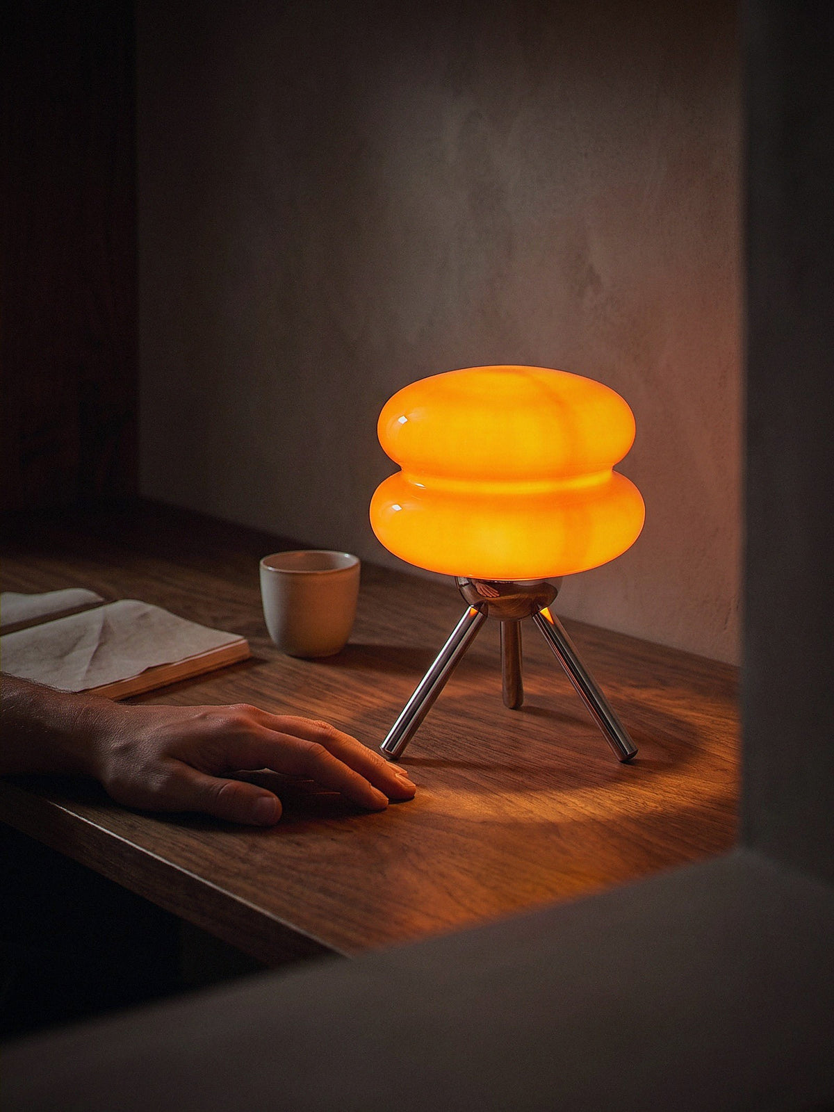 A hand resting beside Carrara Mini, stacked orange glass rings on a polished chrome tripod, showing its true size