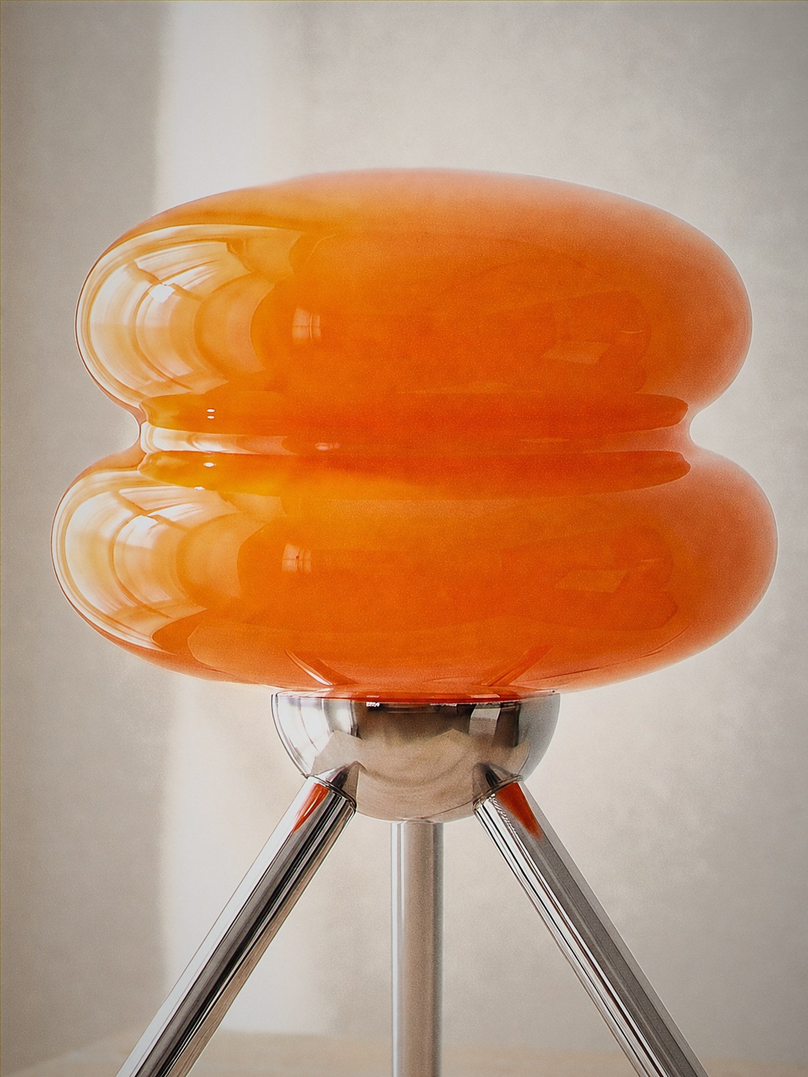 Close detail of Carrara Mini, stacked orange glass rings on a polished chrome tripod