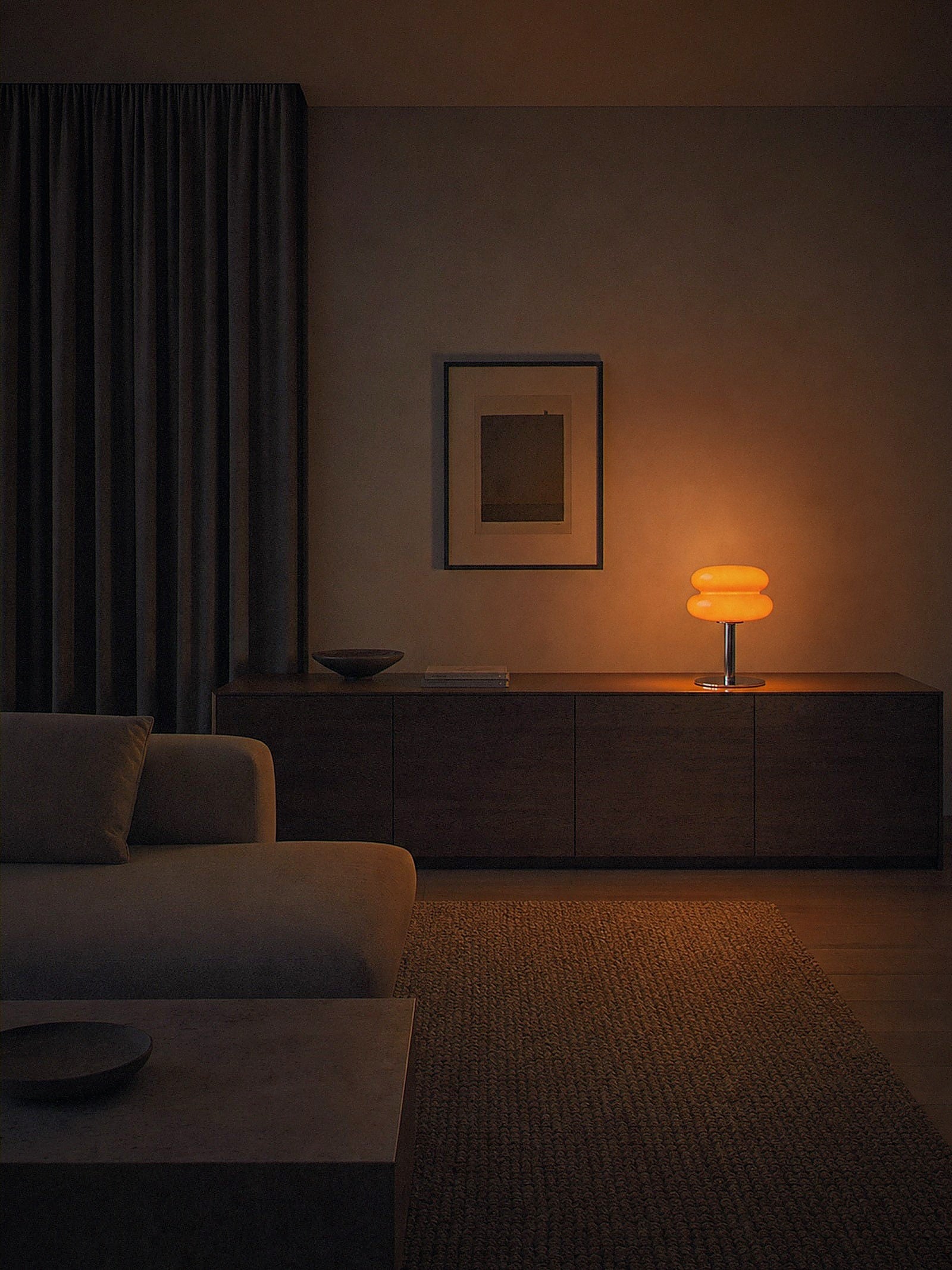 Carrara, two stacked orange glass rings on a polished chrome stem with a round chrome base lit as the only light source in a snug dining corner