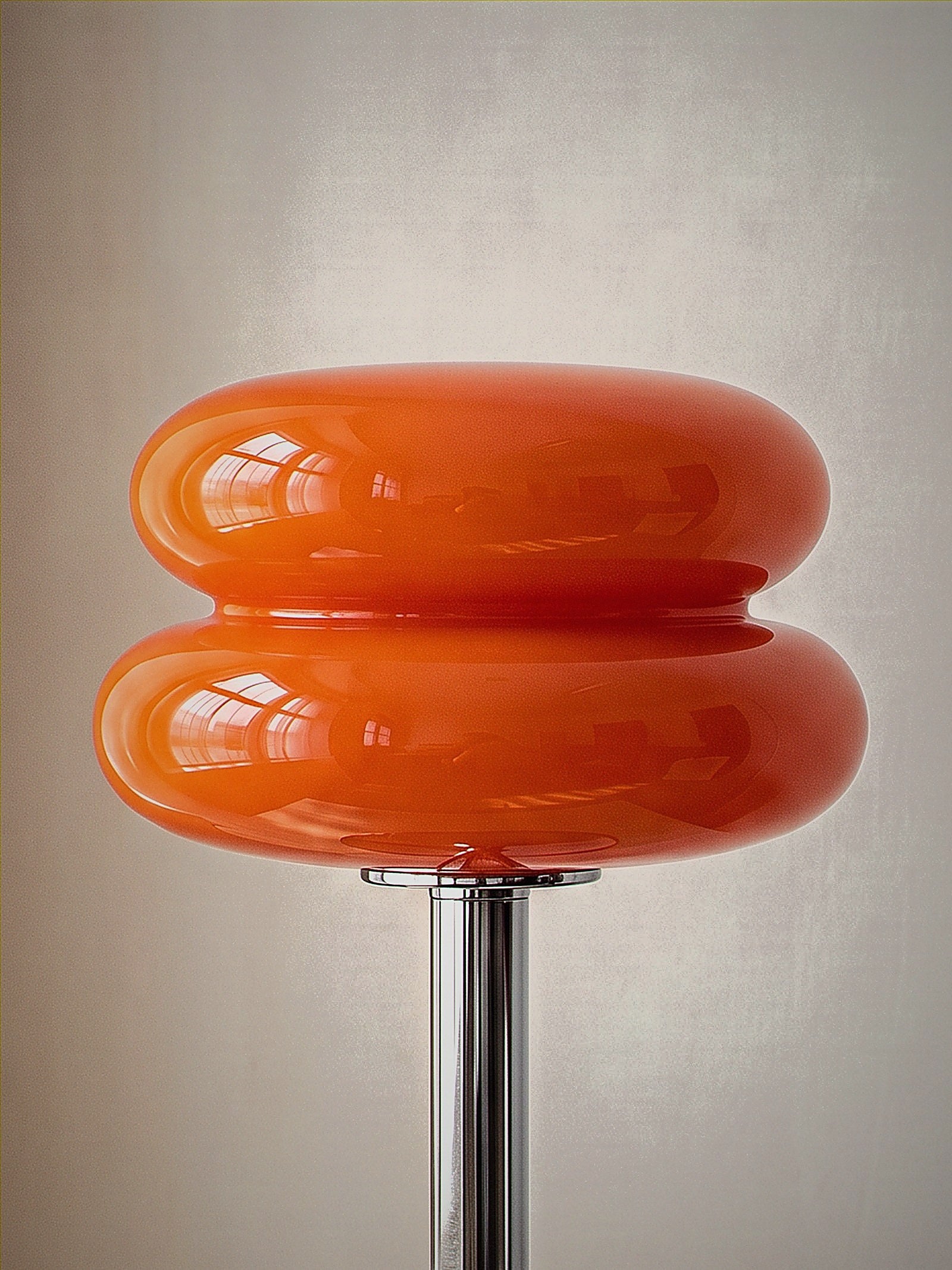 Close detail of Carrara, two stacked orange glass rings on a polished chrome stem with a round chrome base