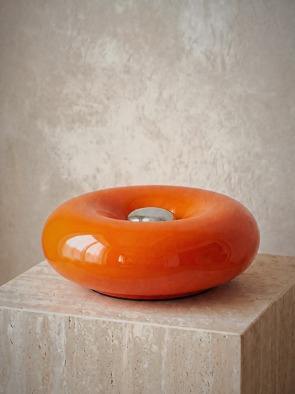 Ember, a solid orange glass ring lying flat with a chrome disc at its centre, unlit