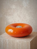 Ember, a solid orange glass ring lying flat with a chrome disc at its centre, unlit