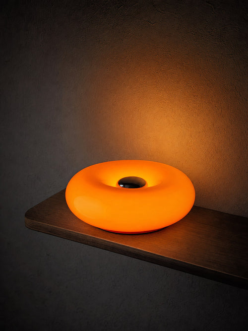 Ember switched on, the whole ring visible, glowing warm on a dark walnut surface at night