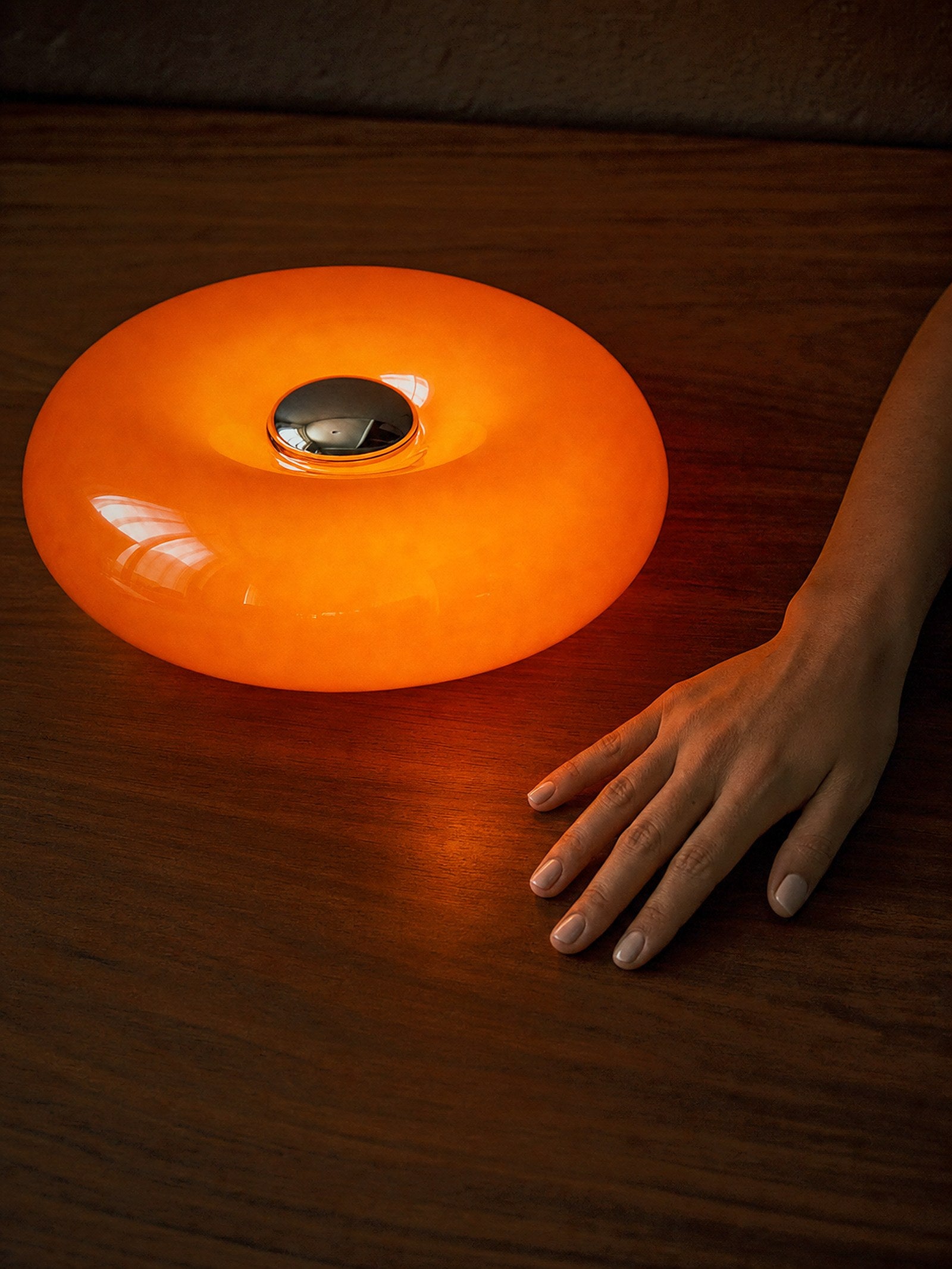 A hand resting on the surface beside the lit Ember, showing its true size