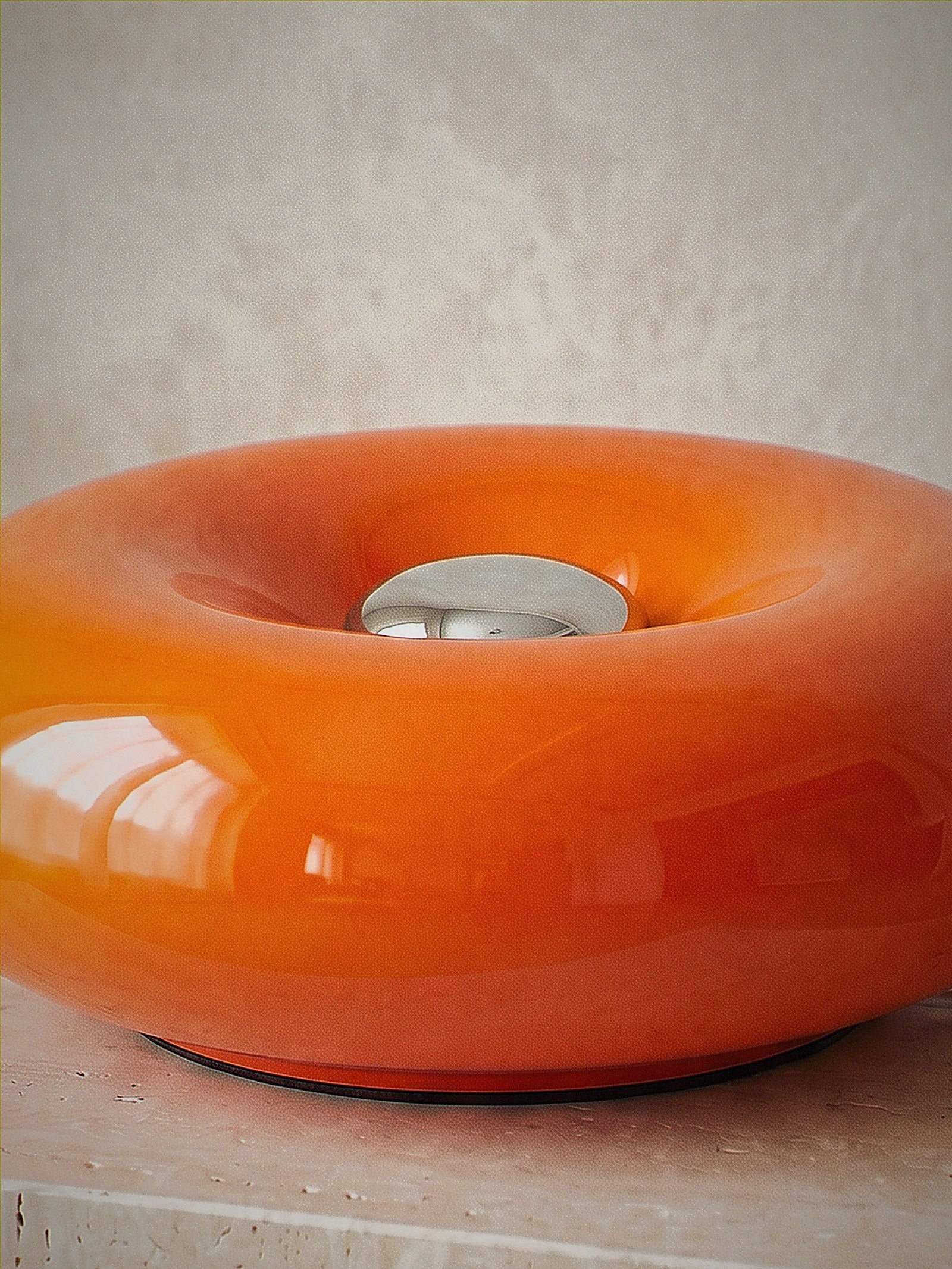 Close detail of Ember, a solid orange glass ring lying flat with a chrome disc at its centre