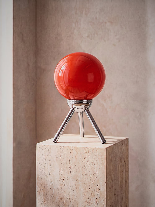 Fjord, a red-orange glass sphere held in a chrome cradle on a three-legged chrome tripod, unlit