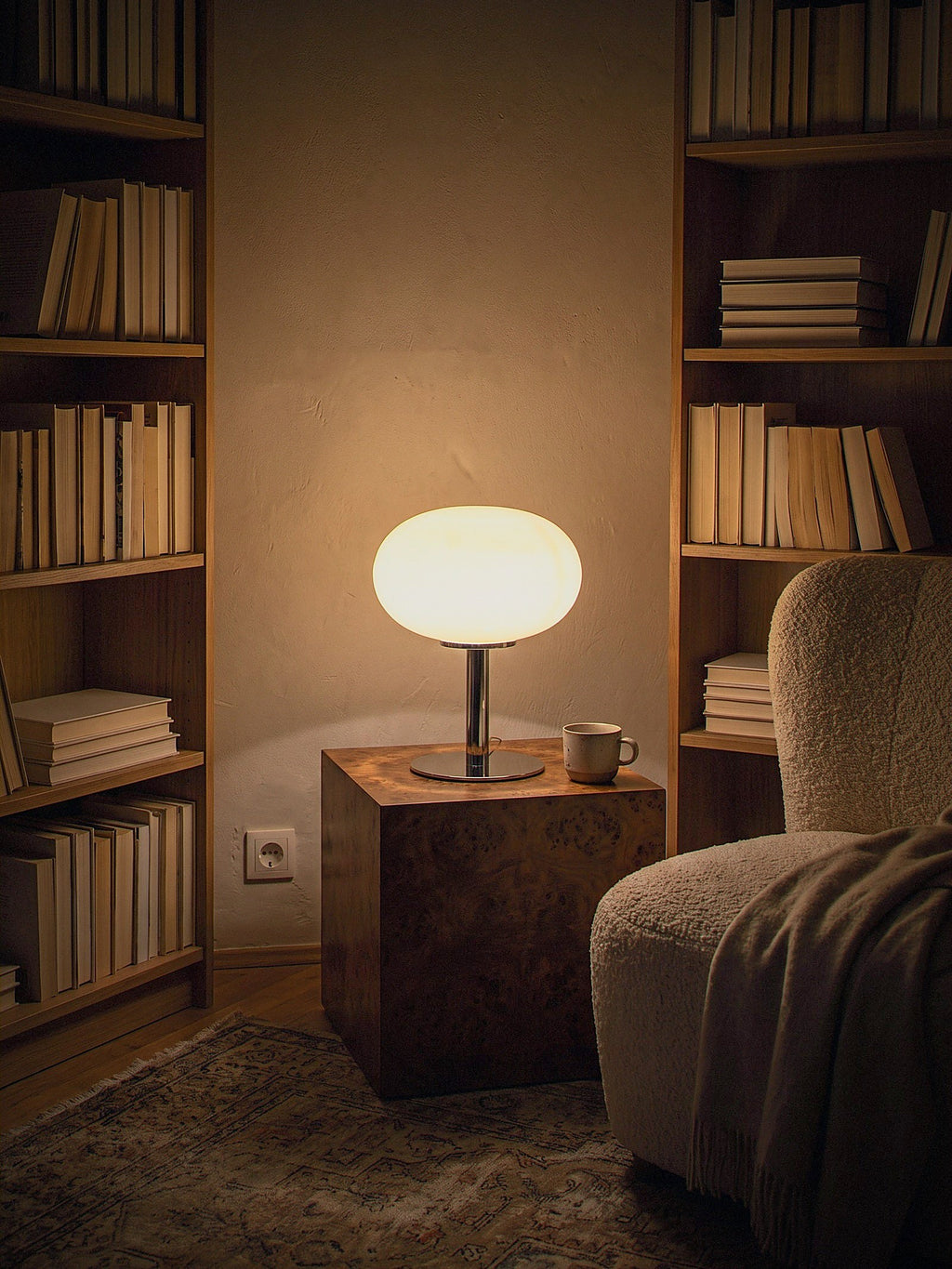 Halo, a soft cream frosted glass dome on a slim polished chrome base lit as the only light source in a small library corner