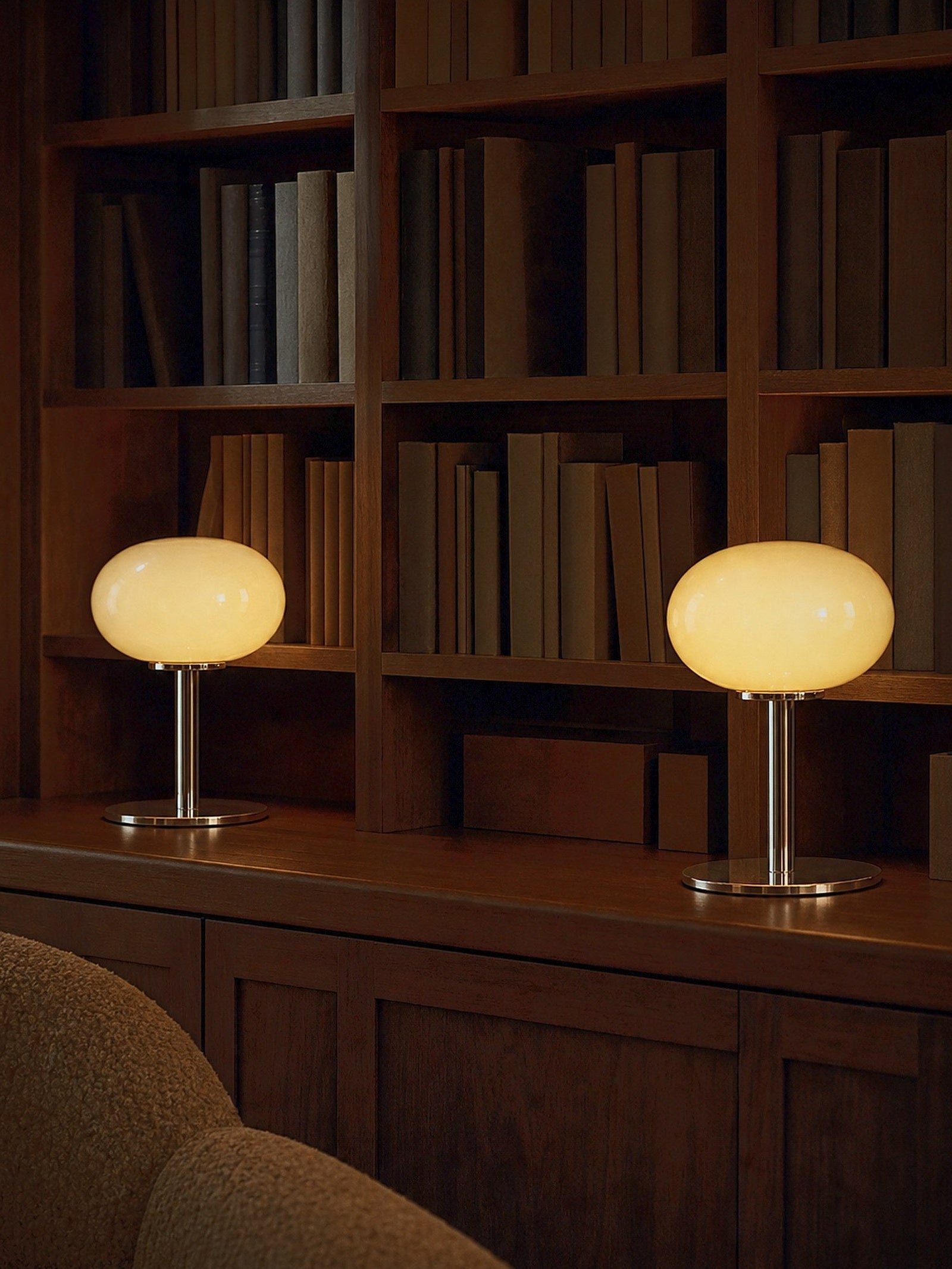 Two Halo lamps lit on a console in front of walnut bookshelves, sold individually
