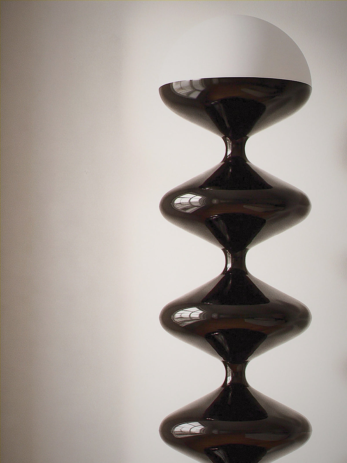 Close detail of Monolith, a tall black lacquered stacked floor lamp with a white glass dome