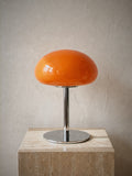 Nimbus, an orange glass dome shade on a slim chrome stem and round chrome base, unlit