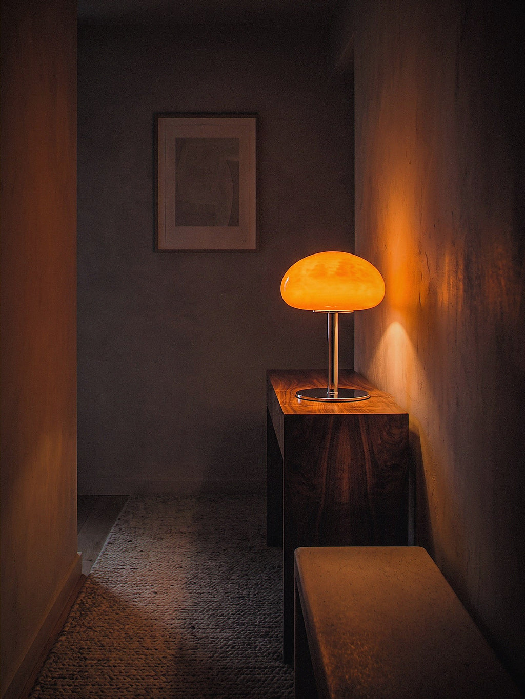 Nimbus, an orange glass dome shade on a slim chrome stem and round chrome base lit as the only light source in a narrow hallway