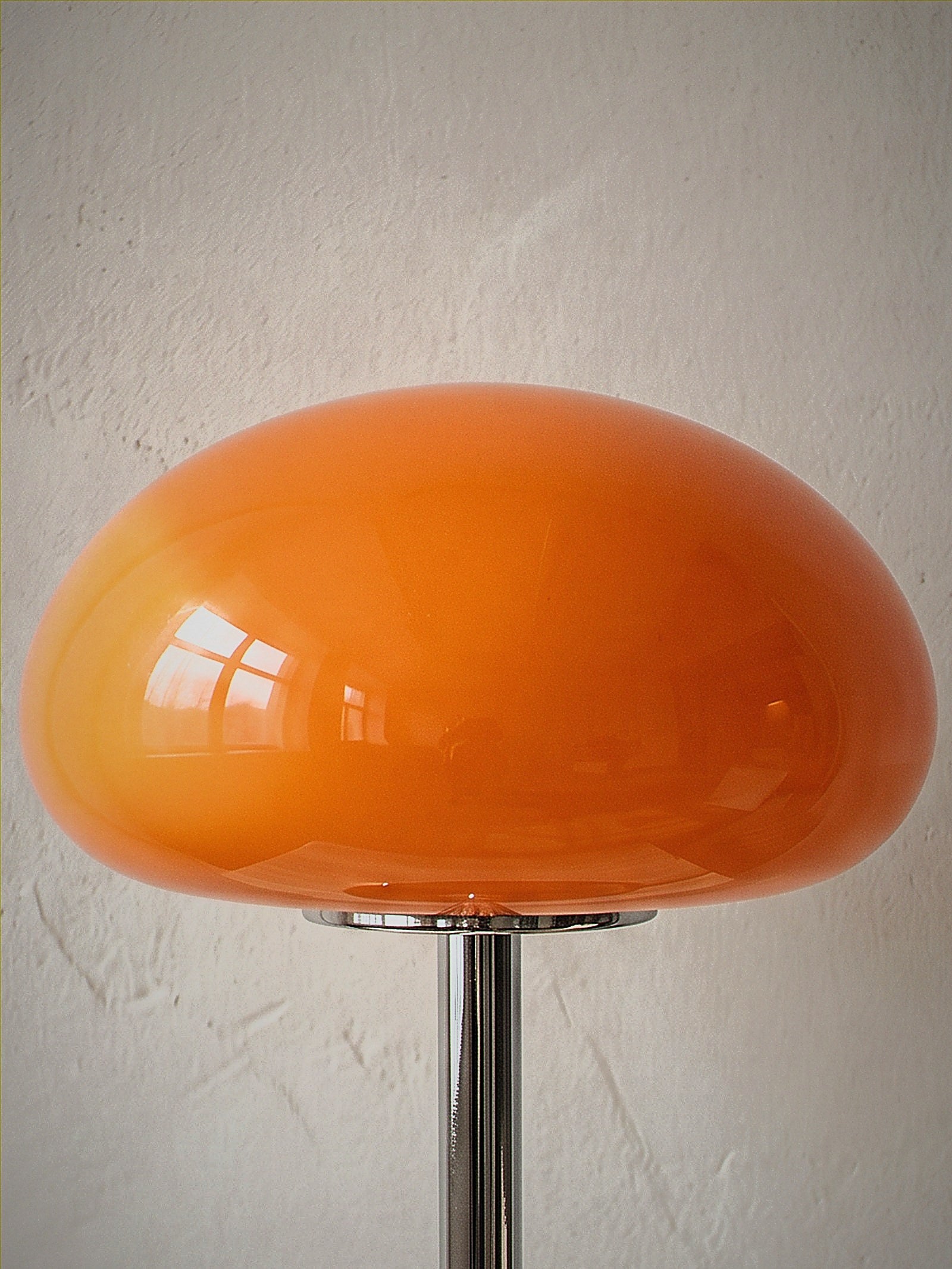 Close detail of Nimbus, an orange glass dome shade on a slim chrome stem and round chrome base