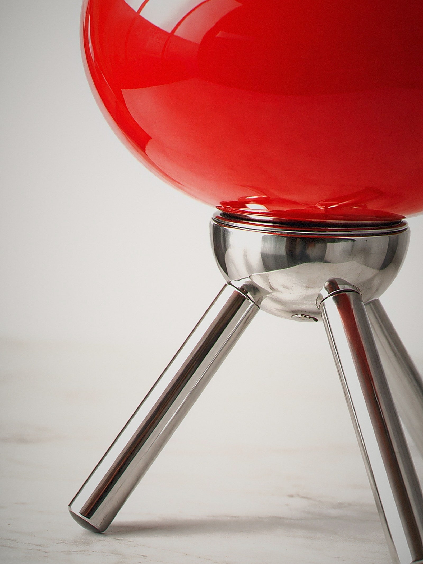 Close detail of Prism, a red glass dome lamp on a polished chrome tripod