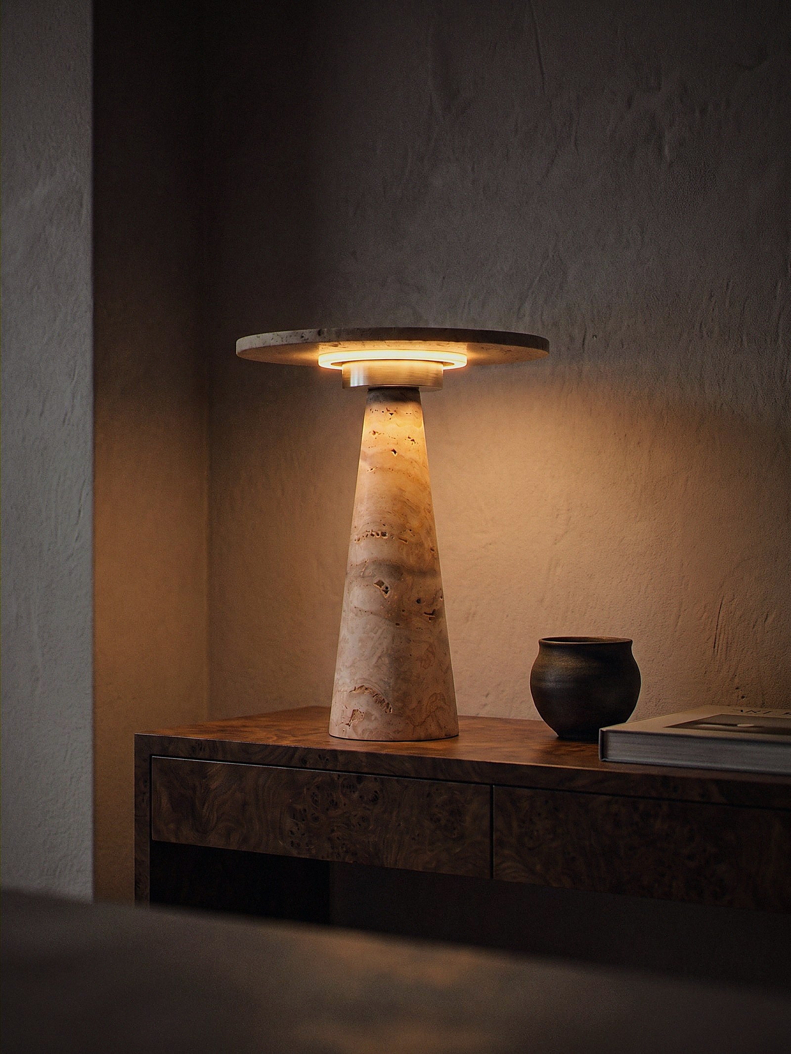 Terrazzo, a travertine cone topped with a travertine disc over a chrome ring diffuser, switched on and glowing warm in an entry hall niche at night
