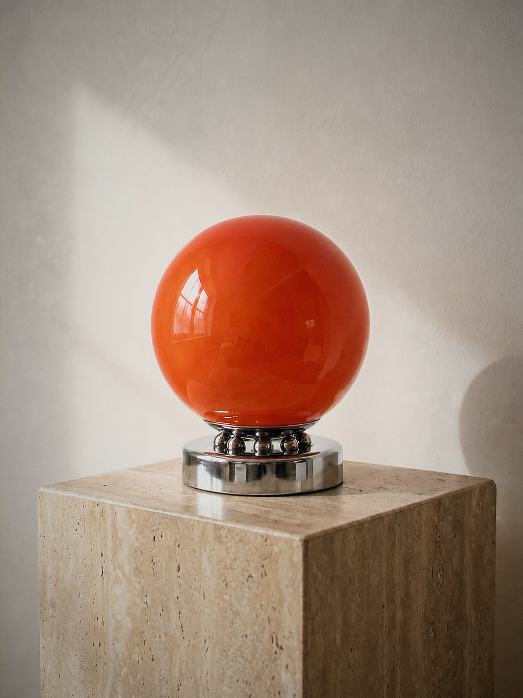 Whisper, an orange glass sphere on a chrome base ringed with polished chrome spheres, unlit