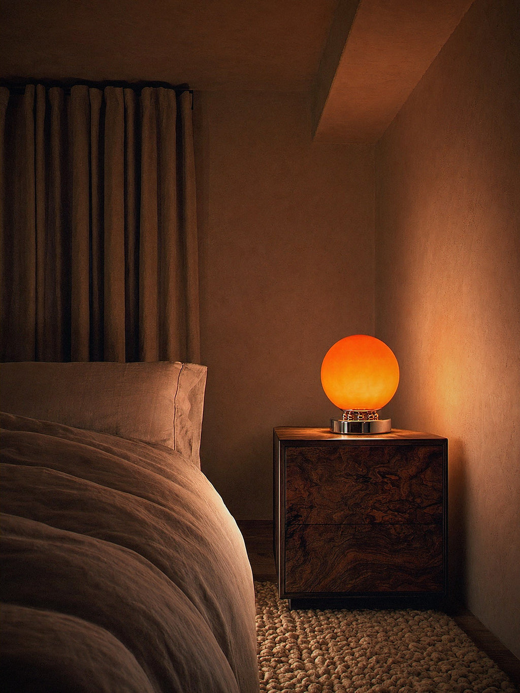 Whisper, an orange glass sphere on a chrome base ringed with polished chrome spheres lit as the only light source in a compact bedroom