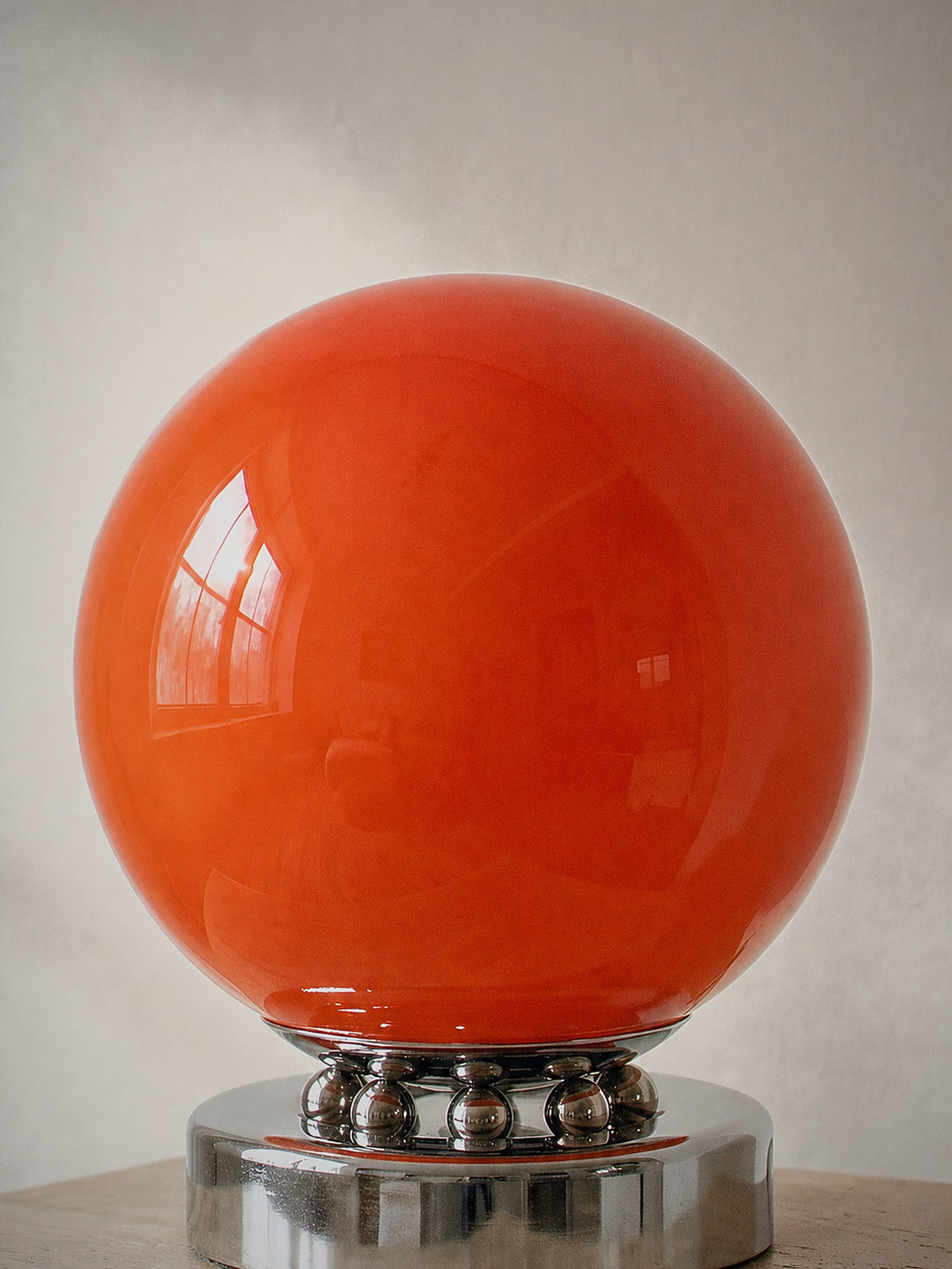Close detail of Whisper, an orange glass sphere on a chrome base ringed with polished chrome spheres