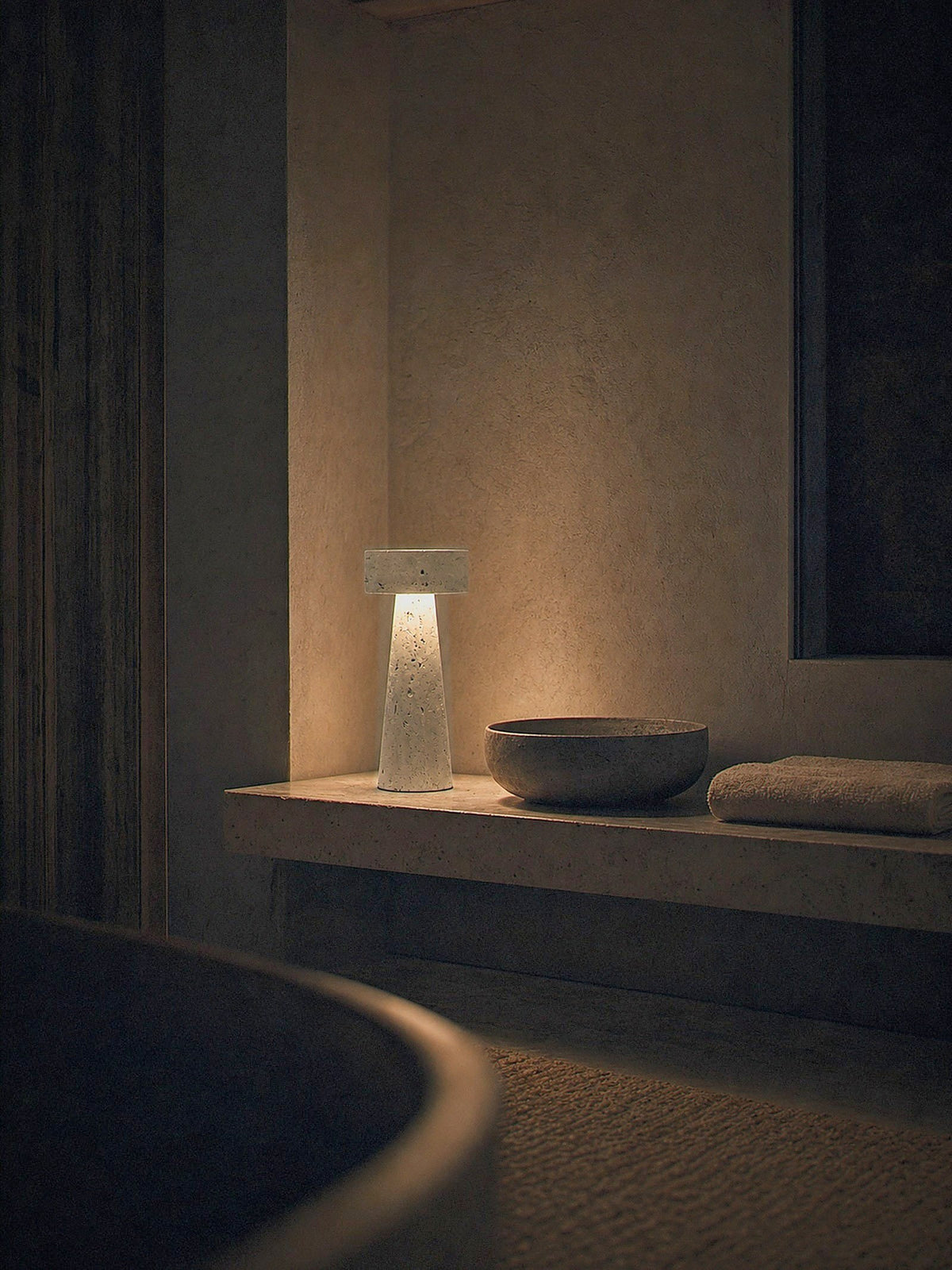 Zen, a tapered travertine column topped with a stone disc lit as the only light source in a calm bedside corner