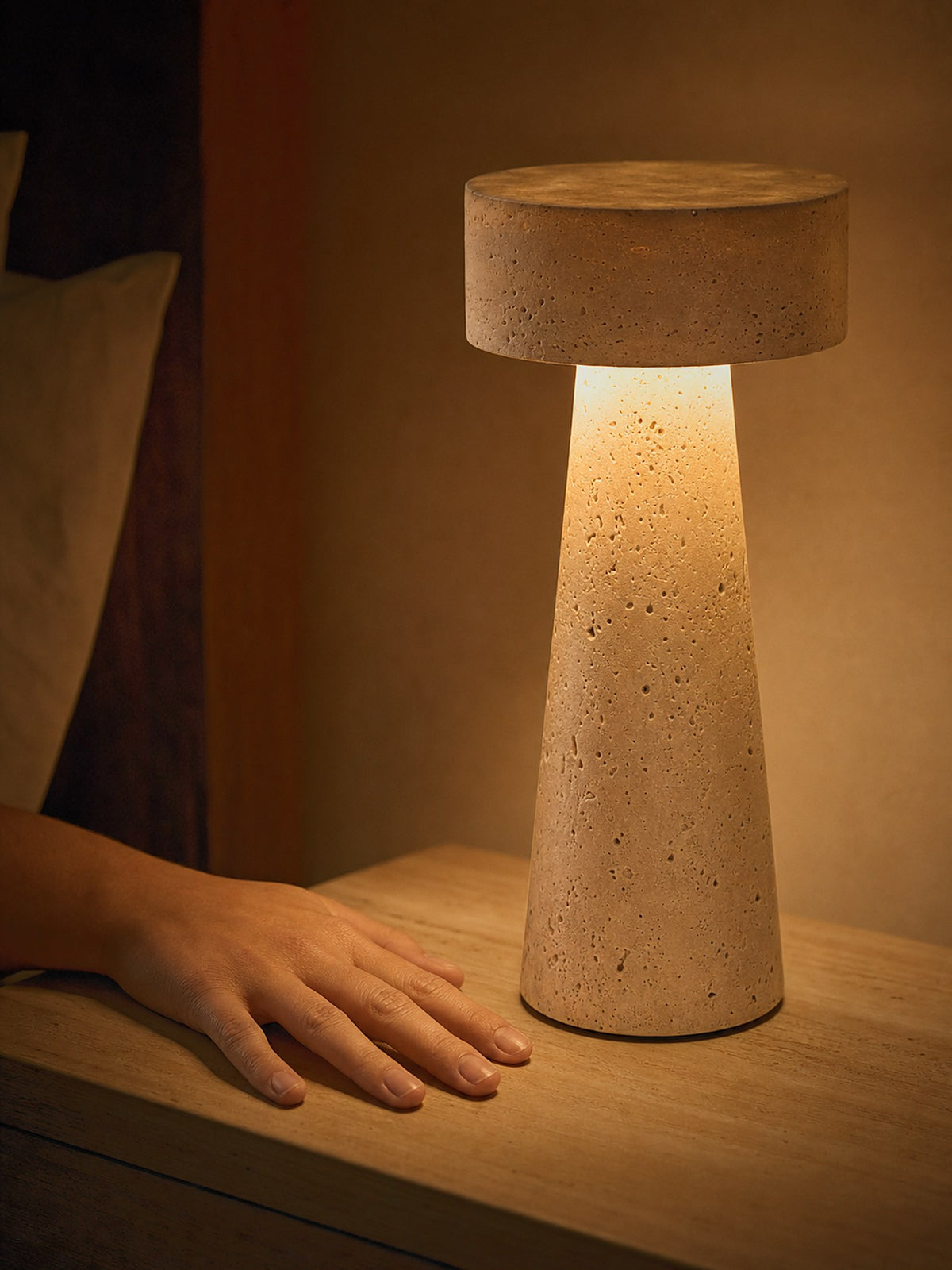 A hand resting beside Zen, a tapered travertine column topped with a stone disc, showing its true size